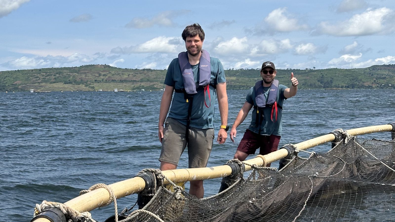 Floris van Rijn and Sam Brown on the walkway of a tilapia cage, Lake Victoria behind them